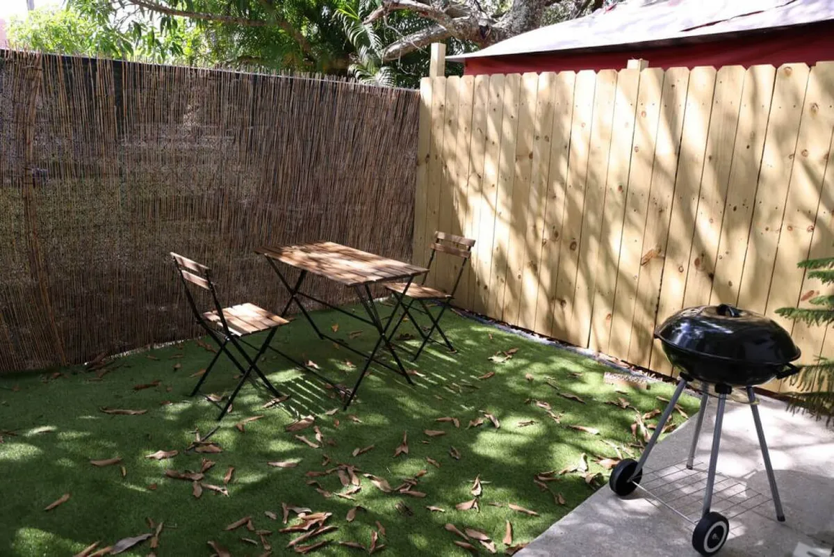 A cozy outdoor setup with a wooden table and foldable chairs under the open sky, next to a grill and a bamboo privacy screen. The setting is ideal for barbecuing, outdoor dining, and relaxed gatherings with friends or family.