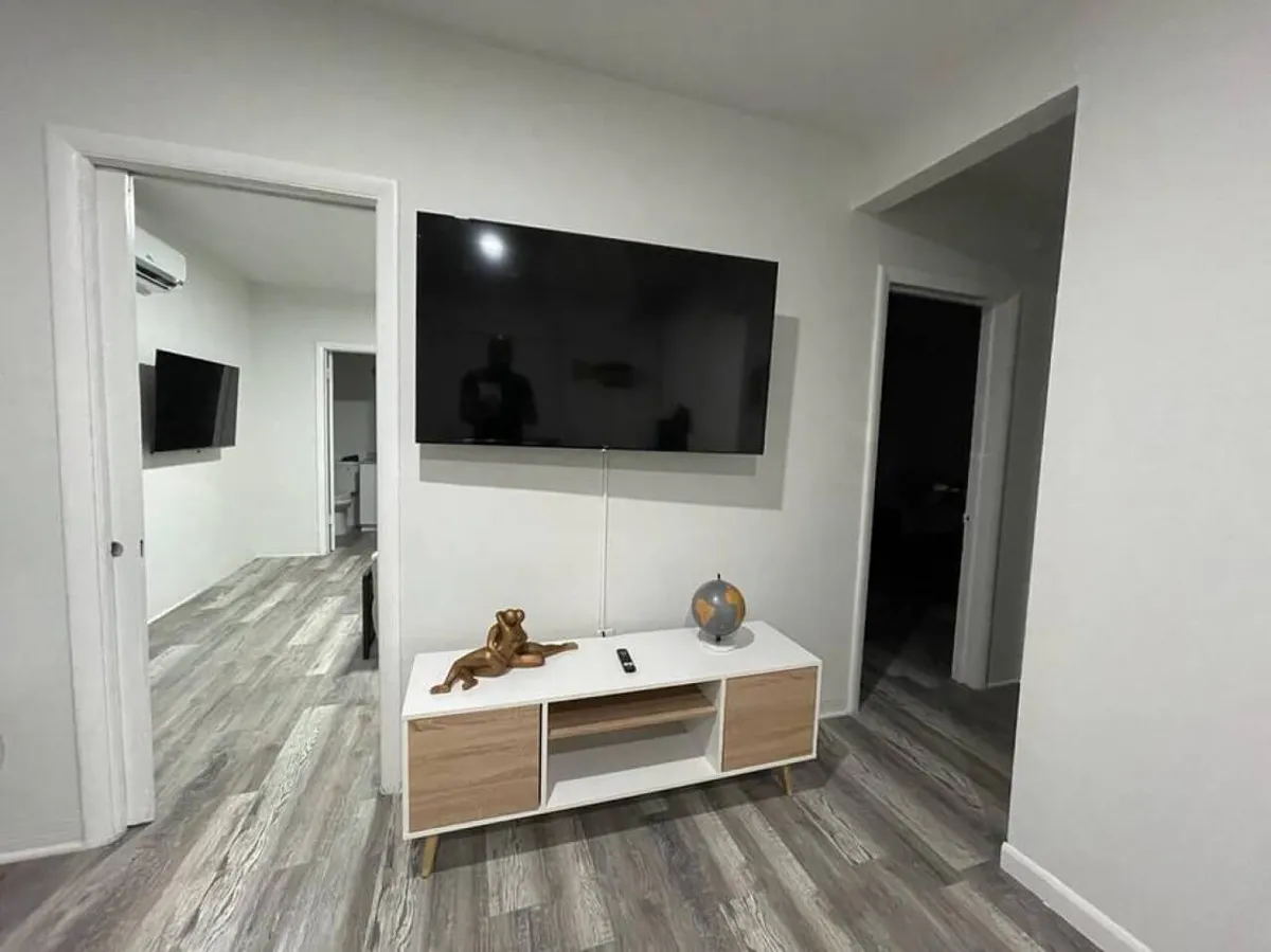 This interior image highlights a large flat-screen TV mounted on the wall above a modern TV console with decorative items. Visible doorways lead to other rooms, suggesting easy movement between spaces. The overall look is functional, calm, and welcoming.
